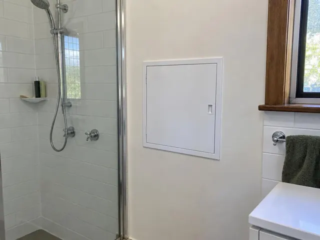 Bathroom wall with a small access panel beside a shower and tiled vanity area in Farley